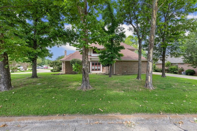 view of property hidden behind natural elements featuring a front lawn, an attached garage, brick siding, and driveway