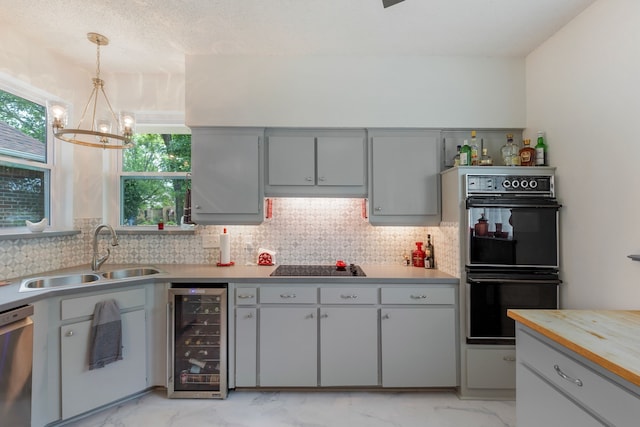 kitchen with wooden counters, black appliances, sink, decorative light fixtures, and beverage cooler