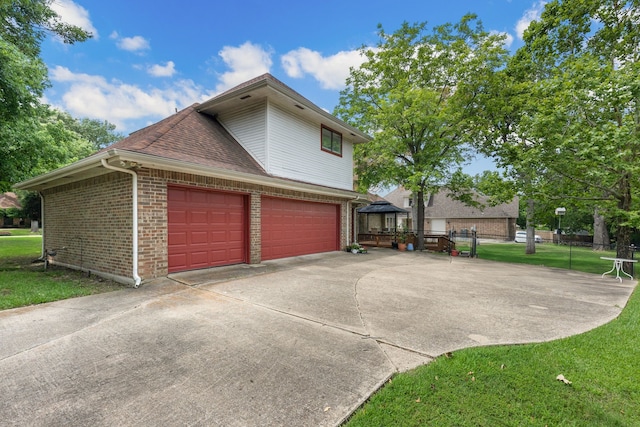 view of side of home featuring a lawn, driveway, a gazebo, roof with shingles, and brick siding
