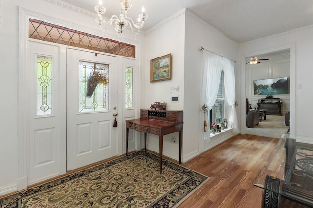 entrance foyer with ceiling fan with notable chandelier, wood-type flooring, and crown molding