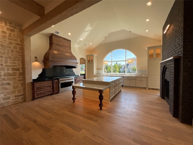 interior space with light wood-type flooring, a kitchen bar, custom exhaust hood, a brick fireplace, and decorative light fixtures