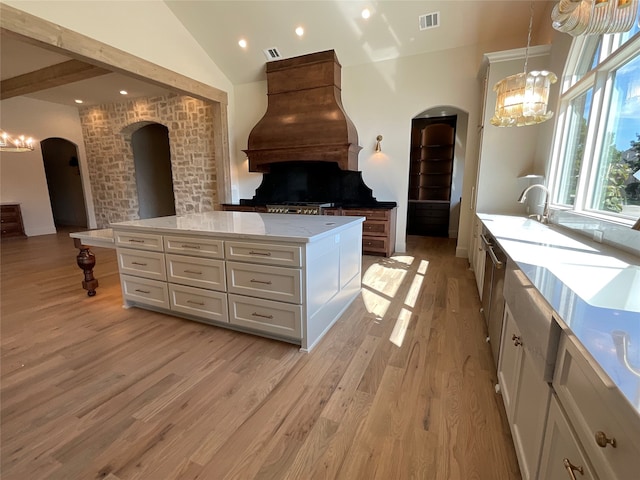 kitchen with vaulted ceiling, white cabinets, a kitchen island, light wood-type flooring, and decorative light fixtures