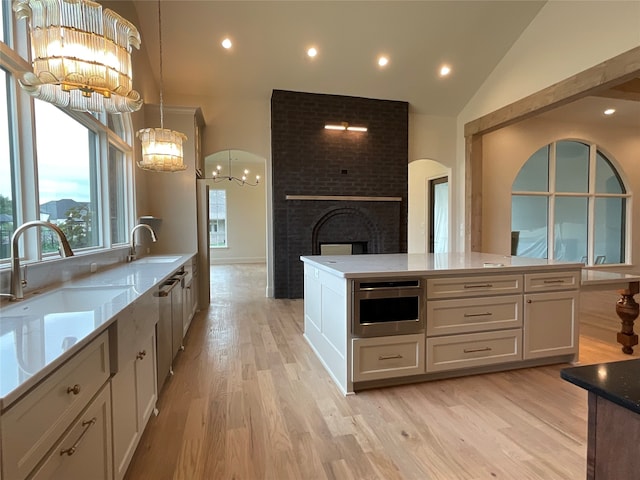 kitchen with white cabinets, vaulted ceiling, hanging light fixtures, a fireplace, and an inviting chandelier