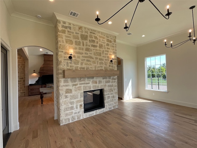 unfurnished living room featuring a notable chandelier, a fireplace, ornamental molding, and hardwood / wood-style flooring