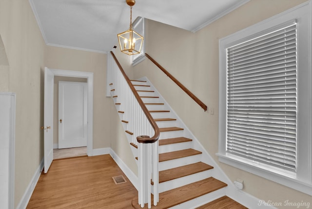 stairway featuring a chandelier, wood-type flooring, and crown molding