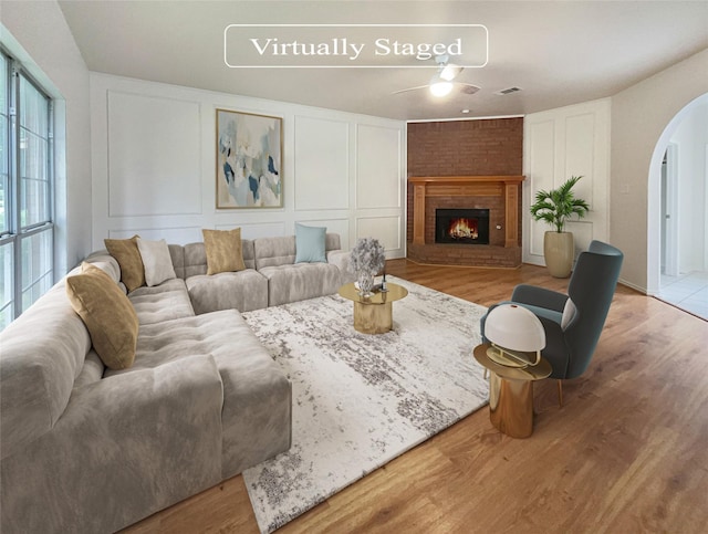 living room featuring a brick fireplace, ceiling fan, and light wood-type flooring