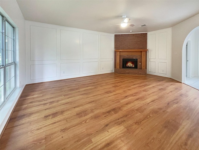 unfurnished living room featuring light wood-type flooring, a brick fireplace, a wealth of natural light, and ceiling fan