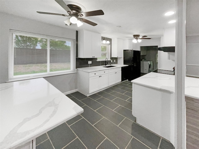 kitchen featuring white cabinets, black fridge, sink, separate washer and dryer, and light stone counters