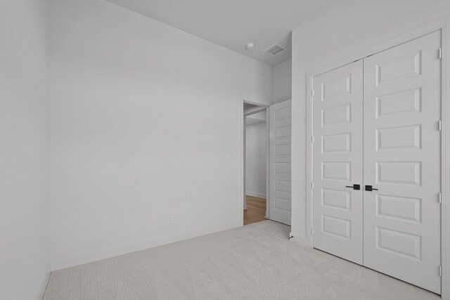 unfurnished bedroom with light colored carpet and a closet