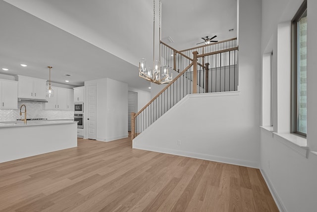 unfurnished living room featuring ceiling fan with notable chandelier, light hardwood / wood-style floors, and sink