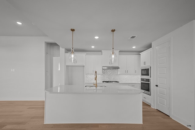 kitchen with a center island with sink, white cabinets, sink, light wood-type flooring, and stainless steel appliances