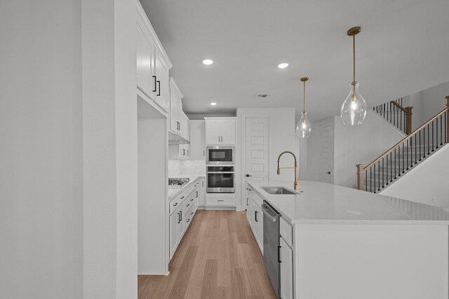 kitchen featuring appliances with stainless steel finishes, pendant lighting, light hardwood / wood-style floors, white cabinetry, and an island with sink