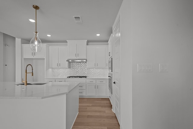 kitchen featuring stainless steel appliances, sink, pendant lighting, light hardwood / wood-style floors, and white cabinetry