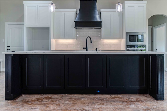 kitchen featuring premium range hood, a kitchen island with sink, and white cabinets