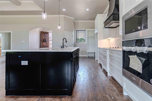 kitchen with wall chimney exhaust hood, sink, decorative light fixtures, a center island with sink, and white cabinetry