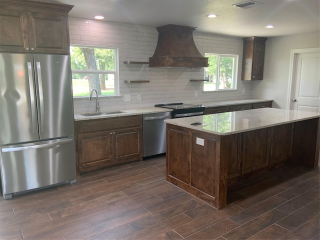 kitchen with backsplash, sink, light stone counters, custom range hood, and stainless steel appliances