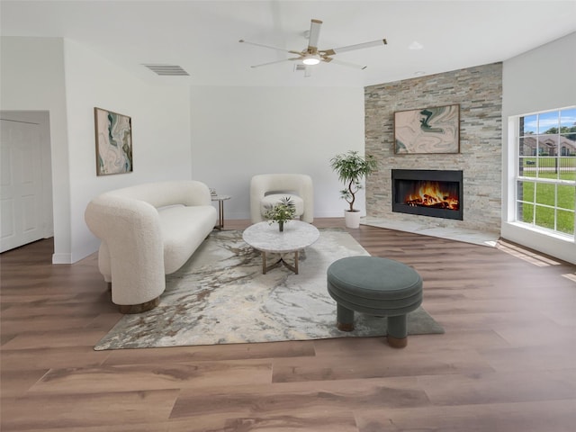 sitting room with wood-type flooring, a stone fireplace, and ceiling fan