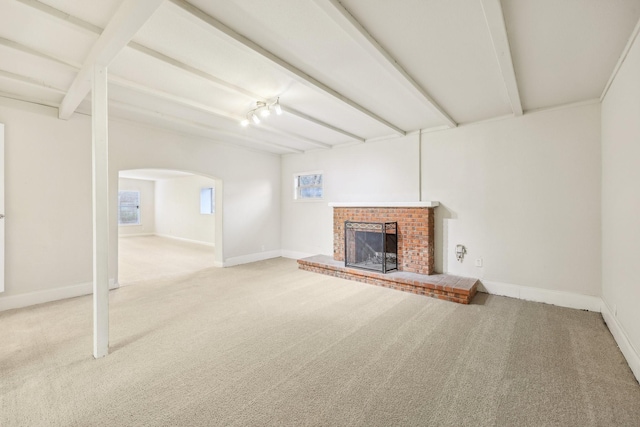 unfurnished living room featuring a brick fireplace, plenty of natural light, beam ceiling, and carpet flooring