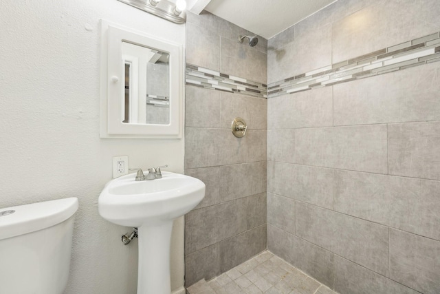 bathroom featuring toilet, tiled shower, and sink