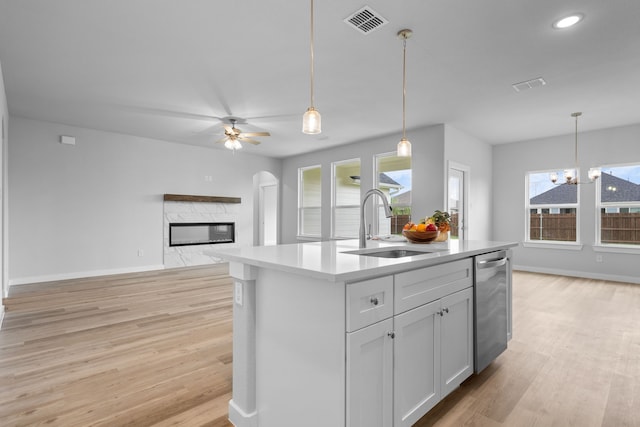 kitchen with decorative light fixtures, ceiling fan with notable chandelier, light hardwood / wood-style floors, a premium fireplace, and a center island with sink