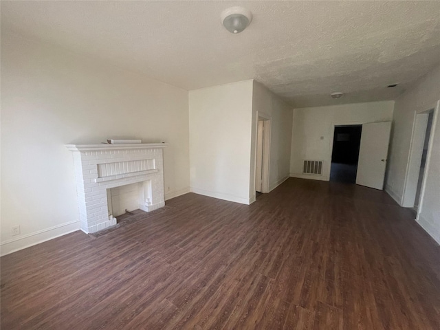 unfurnished living room featuring dark wood-type flooring, a textured ceiling, and a brick fireplace