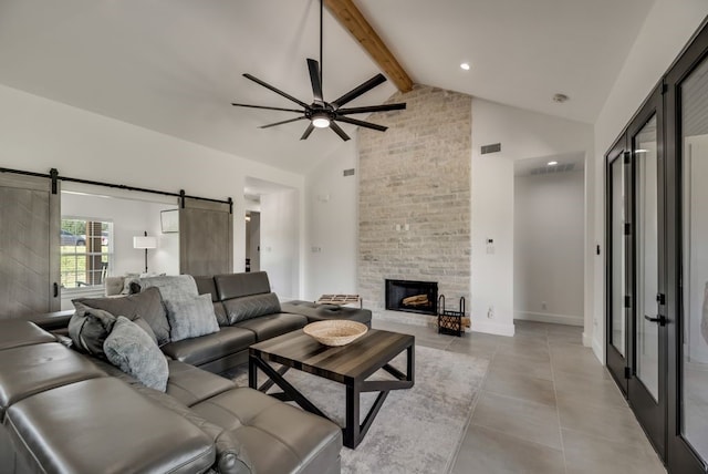 tiled living room featuring a stone fireplace, ceiling fan, beamed ceiling, a barn door, and high vaulted ceiling