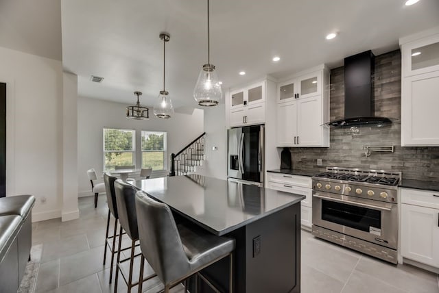 kitchen with a kitchen island, tasteful backsplash, wall chimney exhaust hood, appliances with stainless steel finishes, and light tile floors