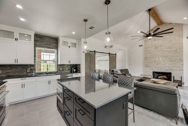 kitchen with ceiling fan, a stone fireplace, white cabinetry, a barn door, and beamed ceiling