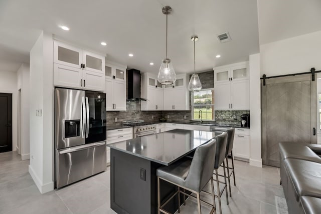 kitchen featuring a center island, wall chimney range hood, appliances with stainless steel finishes, backsplash, and a barn door