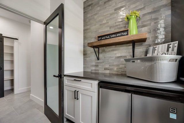 bar featuring a barn door, white cabinets, tasteful backsplash, and light tile floors