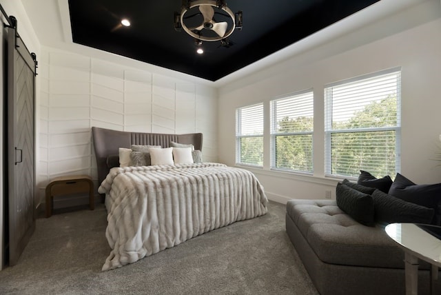 bedroom with a barn door, a tray ceiling, carpet flooring, and a notable chandelier