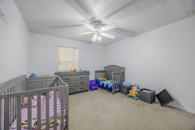 bedroom with a textured ceiling, ceiling fan, a crib, and carpet floors