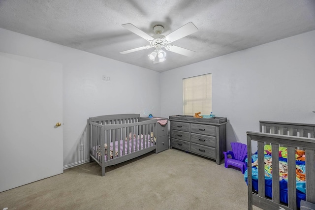 bedroom with a textured ceiling, ceiling fan, light colored carpet, and a crib