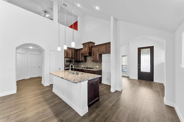 kitchen featuring sink, backsplash, high vaulted ceiling, light stone countertops, and an island with sink