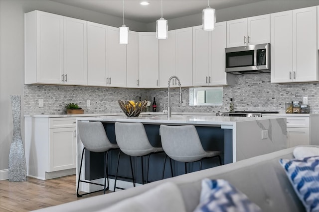 kitchen with white cabinetry, pendant lighting, a kitchen bar, and light hardwood / wood-style flooring