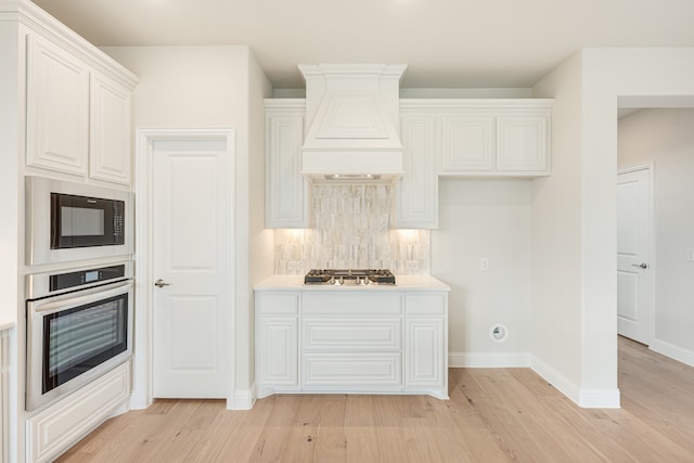 kitchen with white cabinetry, custom exhaust hood, light hardwood / wood-style floors, and stainless steel appliances