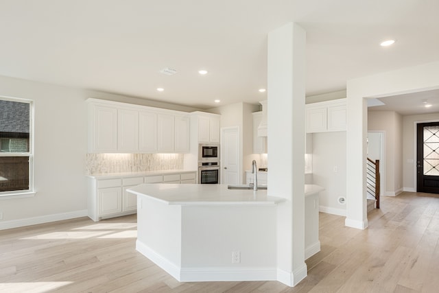 kitchen with stainless steel appliances, decorative backsplash, sink, white cabinetry, and light hardwood / wood-style flooring