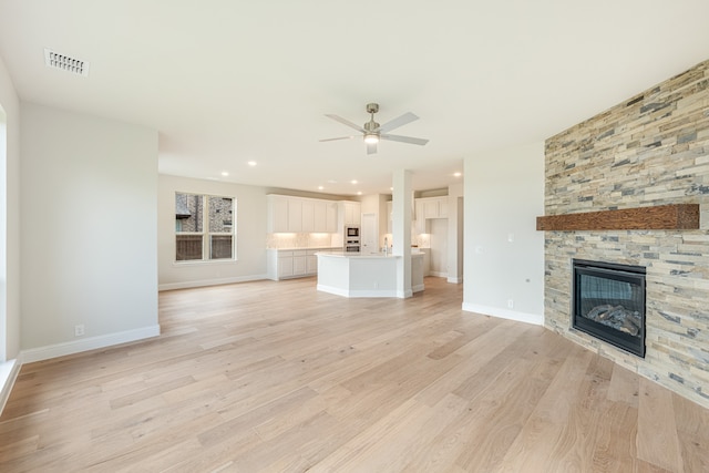 unfurnished living room with ceiling fan, light hardwood / wood-style floors, and a stone fireplace