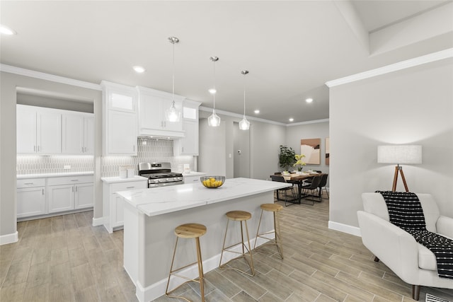 kitchen with decorative backsplash, light stone counters, stainless steel range with gas stovetop, white cabinets, and a kitchen island