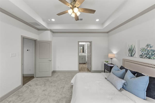 bedroom with ceiling fan, a tray ceiling, light colored carpet, and ensuite bath