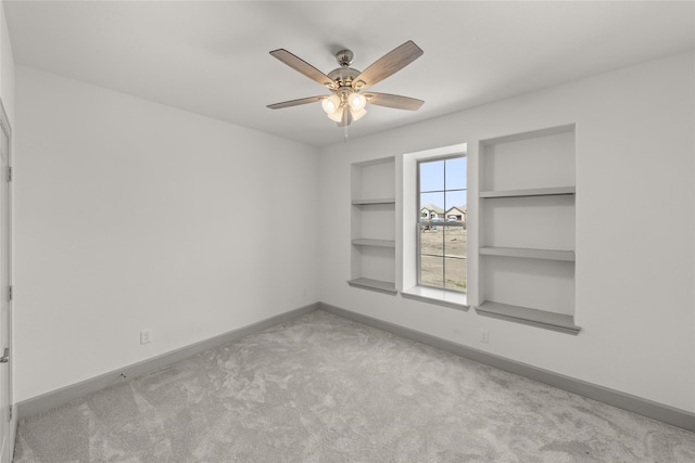 unfurnished room with ceiling fan, built in shelves, and light carpet