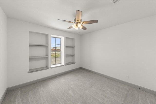 empty room featuring built in features, light colored carpet, and ceiling fan