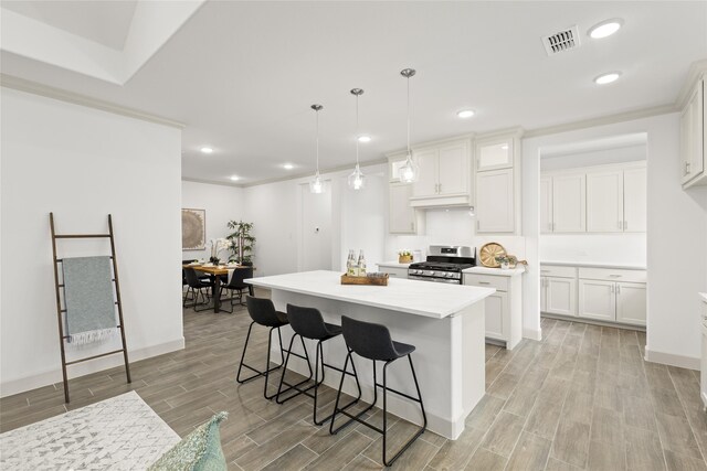 kitchen featuring light hardwood / wood-style flooring, white cabinets, pendant lighting, and stainless steel gas range oven