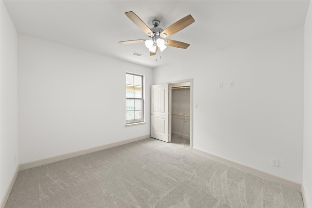 unfurnished bedroom with a spacious closet, ceiling fan, light colored carpet, and a closet