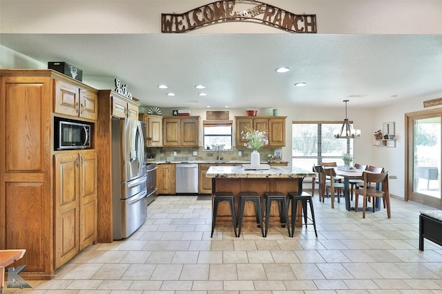 kitchen featuring appliances with stainless steel finishes, a healthy amount of sunlight, backsplash, and pendant lighting