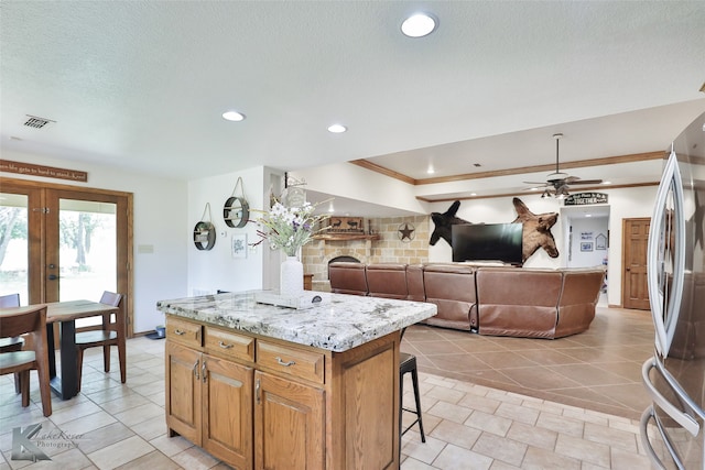 kitchen with a center island, french doors, light stone countertops, stainless steel fridge, and ceiling fan