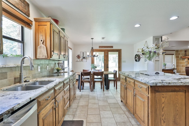 kitchen with light stone countertops, backsplash, pendant lighting, dishwasher, and light tile floors