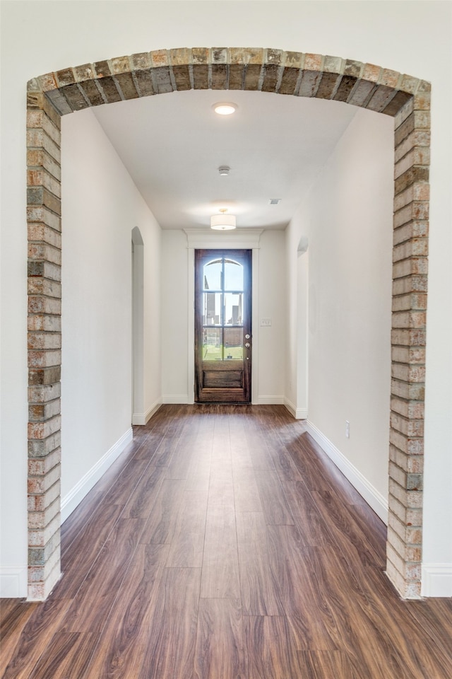 entryway featuring arched walkways, dark wood-type flooring, and baseboards