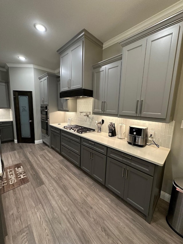 kitchen featuring stainless steel appliances, hardwood / wood-style floors, ornamental molding, decorative backsplash, and gray cabinets