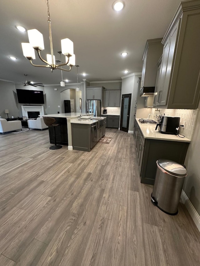 kitchen with hanging light fixtures, stainless steel appliances, an island with sink, tasteful backsplash, and wood-type flooring